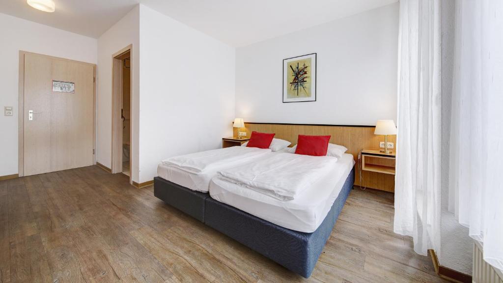 Schlafzimmer mit einem Bett mit weißer Bettwäsche und roten Kissen in der Unterkunft Airport-Hotel Stetten in Leinfelden-Echterdingen