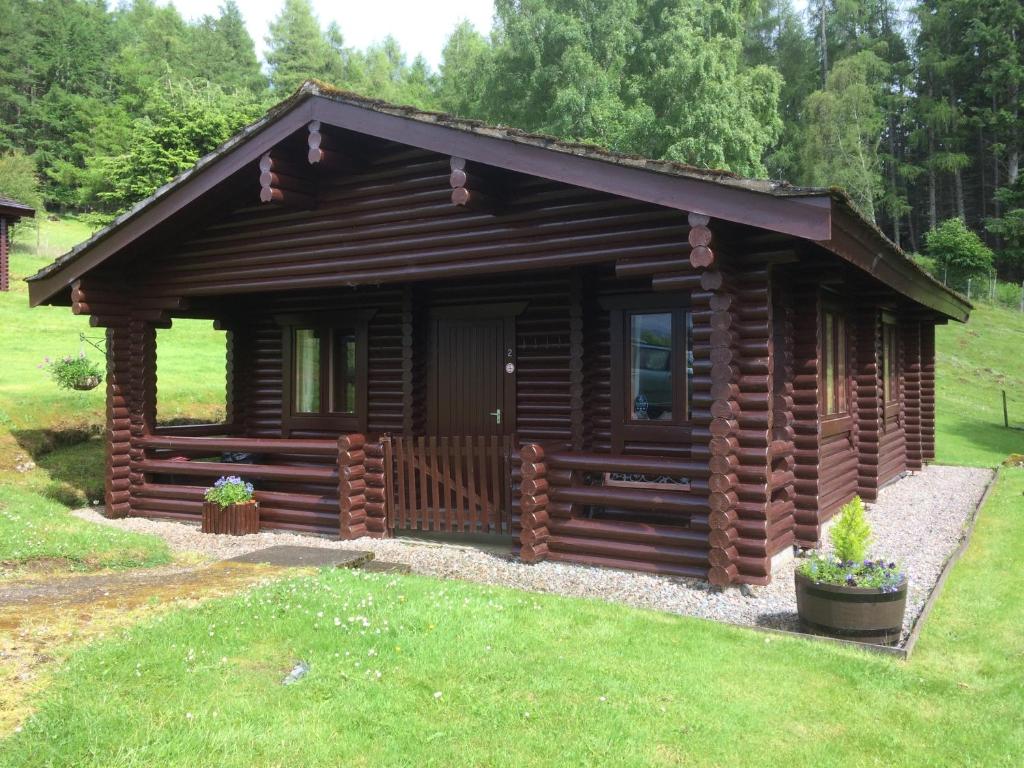 a log cabin in a yard with a green lawn at Highgarry Lodges in Invergarry