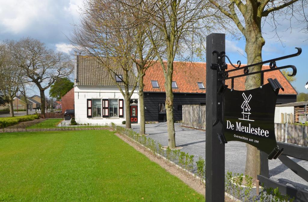 een bord op een paal in een tuin met een huis bij De Meulestee in Ouddorp