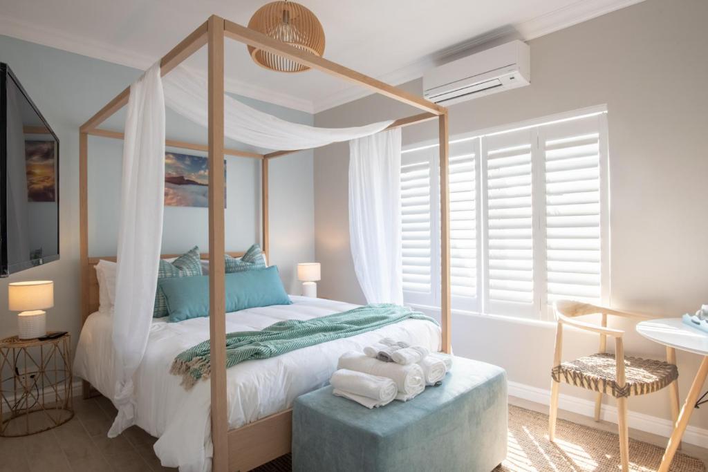 a bedroom with a canopy bed and a chair at Bentley's Guesthouse in Bloubergstrand