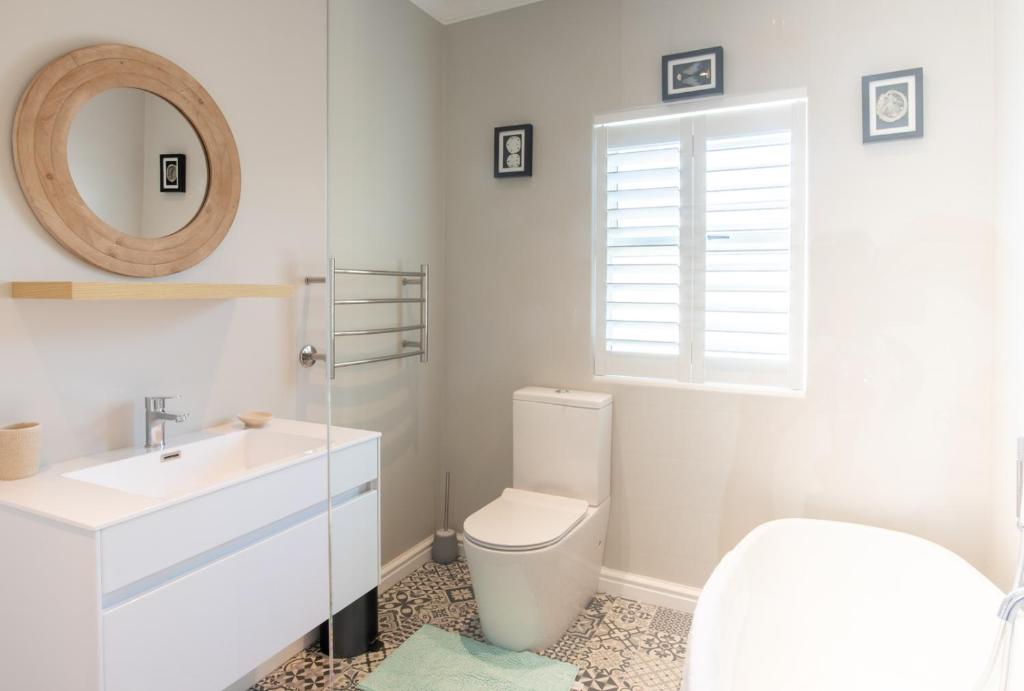a bathroom with a toilet and a sink and a mirror at Bentley's Guesthouse in Bloubergstrand