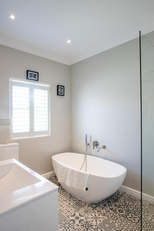 a white bathroom with a tub and a window at Bentley's Guesthouse in Bloubergstrand