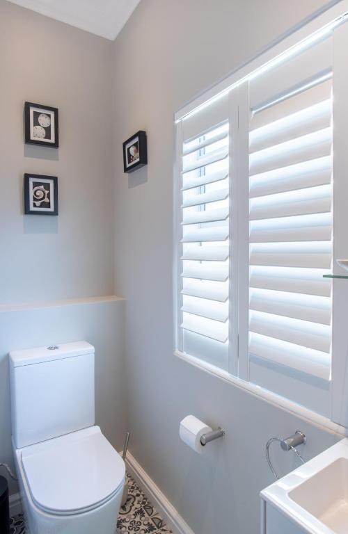 a bathroom with a toilet and a window with blinds at Bentley's Guesthouse in Bloubergstrand