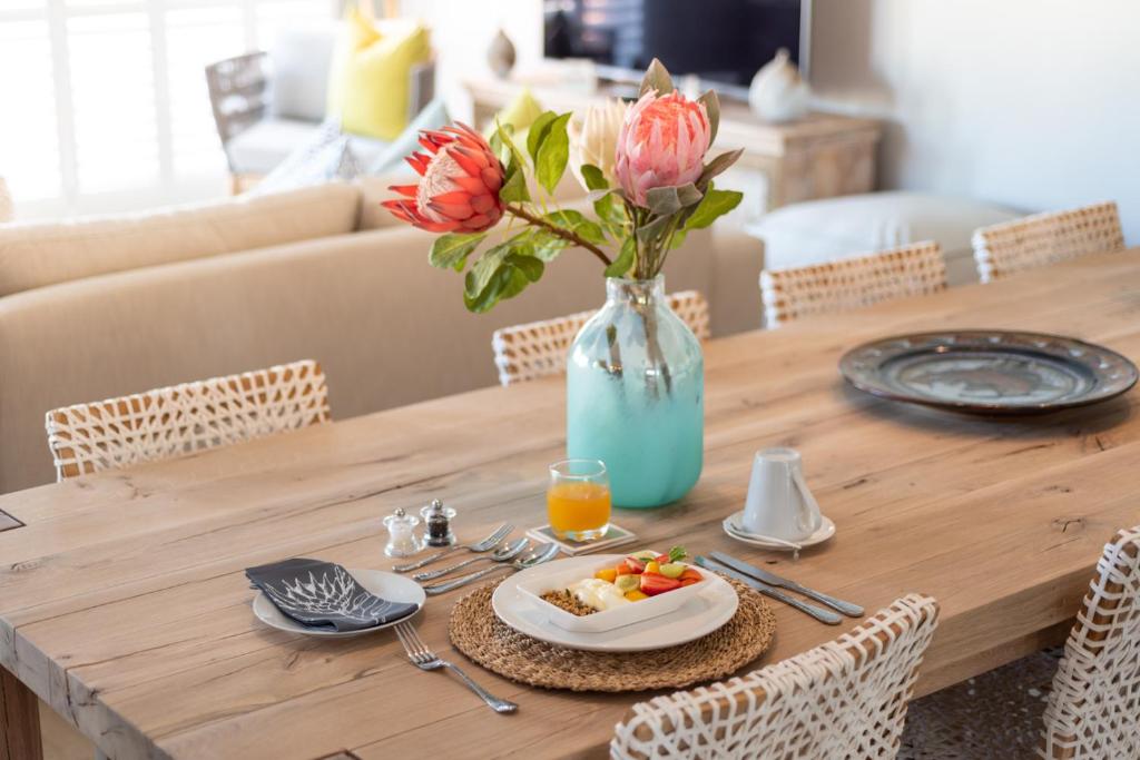 a table with a vase of flowers and a plate of food at Bentley's Guesthouse in Bloubergstrand