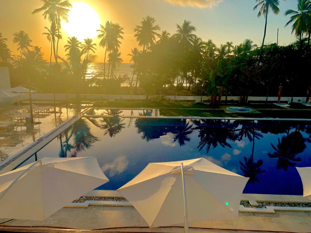 een zwembad met parasols en palmbomen en de zonsondergang bij Oasi Encantada - Beach Resort in Santa Cruz de Barahona