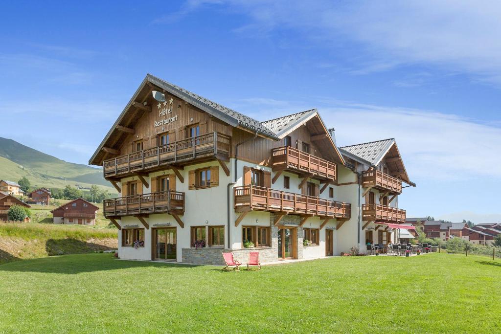 a large house with a green lawn in front of it at Chalet-Hôtel Le Beausoleil, The Originals Relais (Hotel-Chalet de Tradition) in La Toussuire