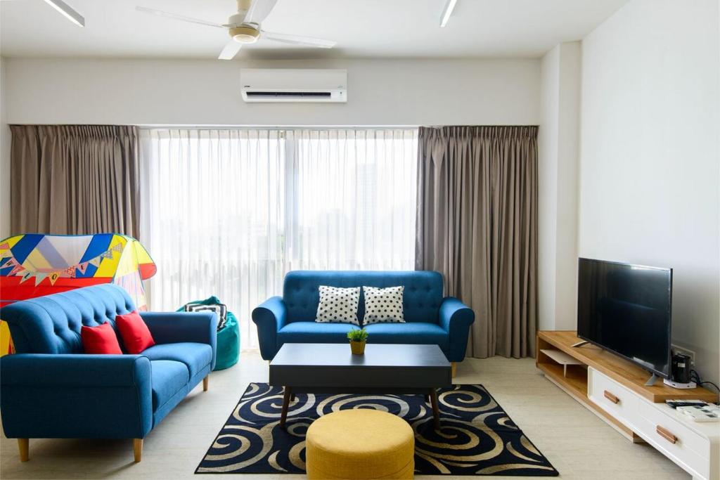a living room with two blue chairs and a tv at By The Sea Beach Front Apartment in Batu Ferringhi