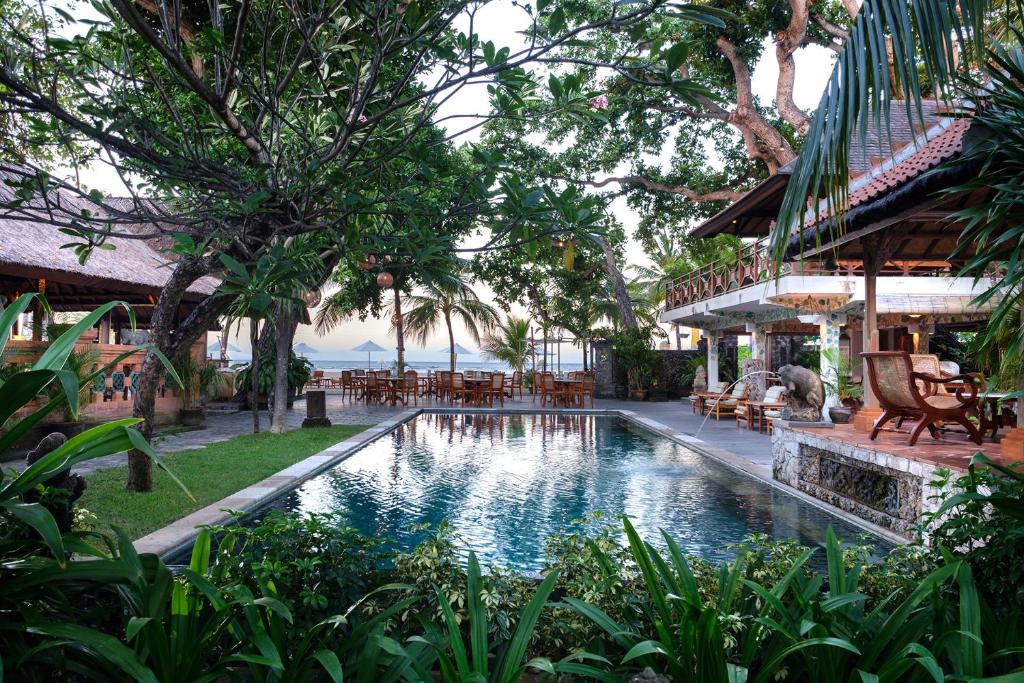 a pool at a resort with tables and chairs at Tandjung Sari Hotel in Sanur