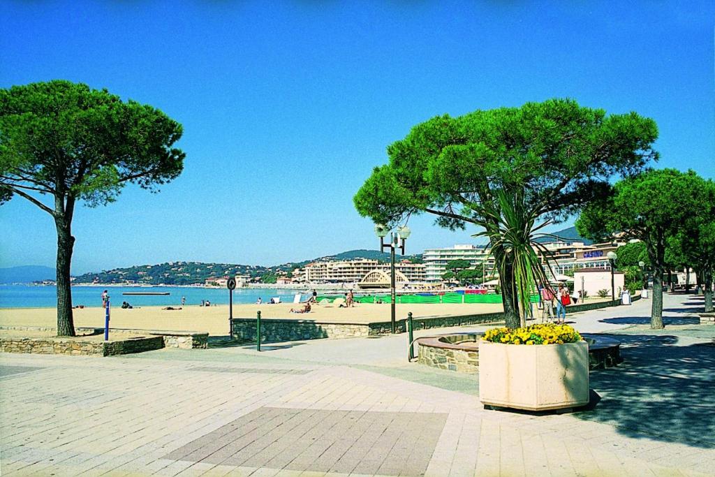 a park with a beach and trees and a bench at Hôtel Lou Paouvadou in Sainte-Maxime