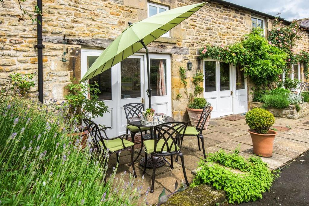 un patio con mesa, sillas y sombrilla en West Cottage, Southlands Farm, Gunnerton en Hexham