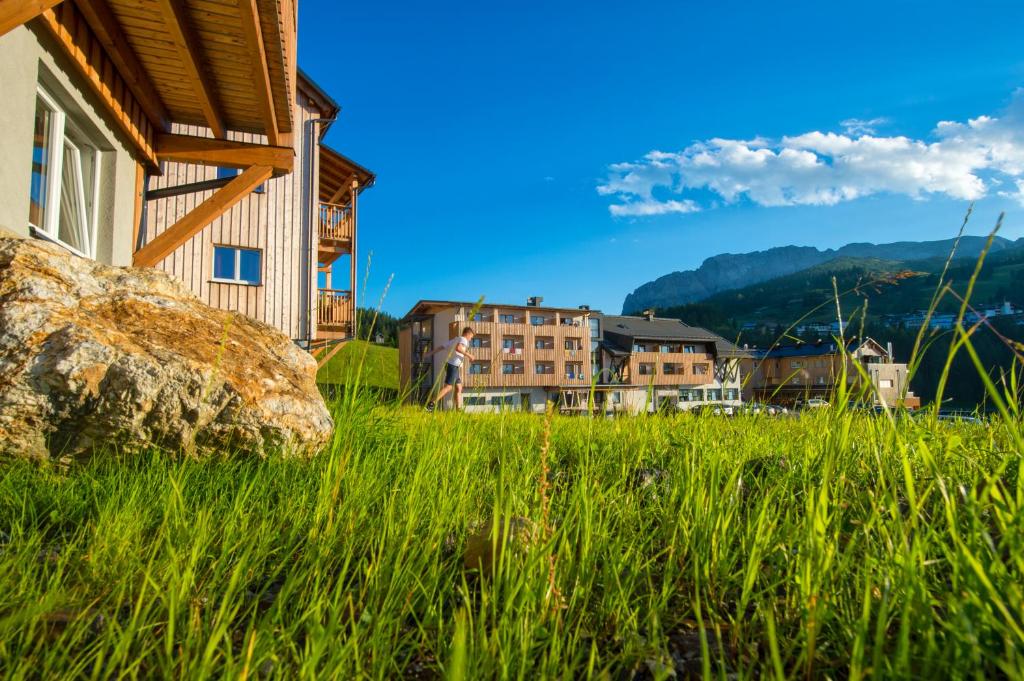 a house in a field of grass with buildings in the background at Almhotel Kärnten in Sonnenalpe Nassfeld