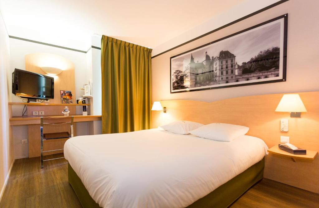 Pokój hotelowy z łóżkiem, biurkiem i telewizorem w obiekcie Hotel inn Grenoble Eybens Parc des Expositions Ex Kyriad w mieście Eybens