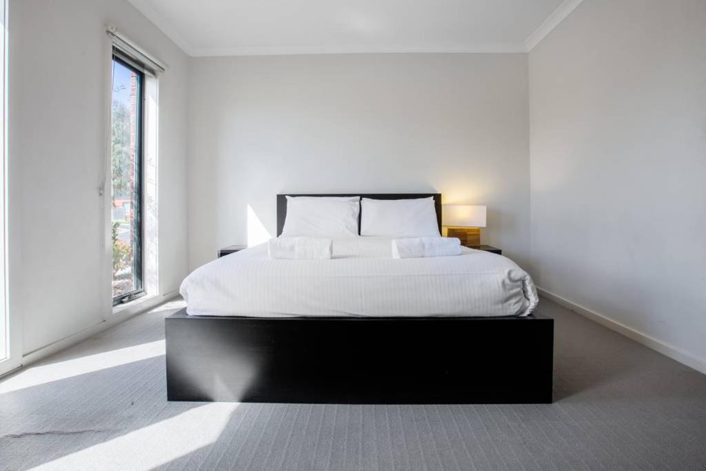 a white bedroom with a large bed and two windows at Holiday Rose in Point Cook