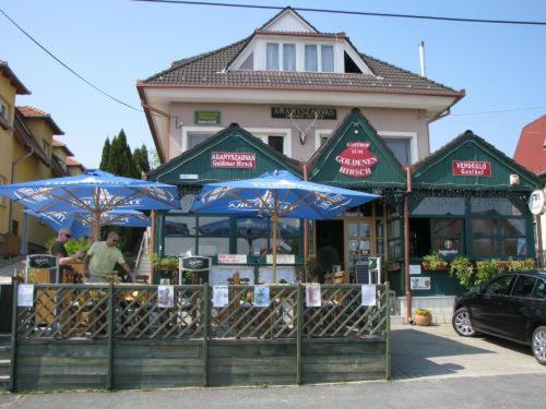 a restaurant with blue umbrellas in front of a building at Aranyszarvas-Goldener Hirsch Pension in Zalakaros