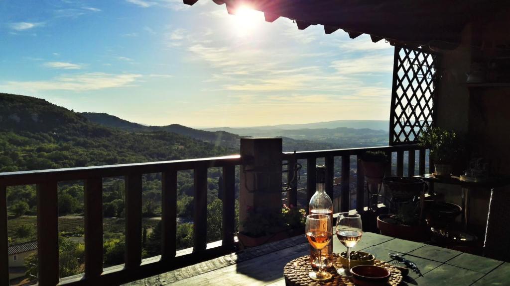a table with wine glasses on a balcony with a view at Entre Terre et Ciel. in Saignon