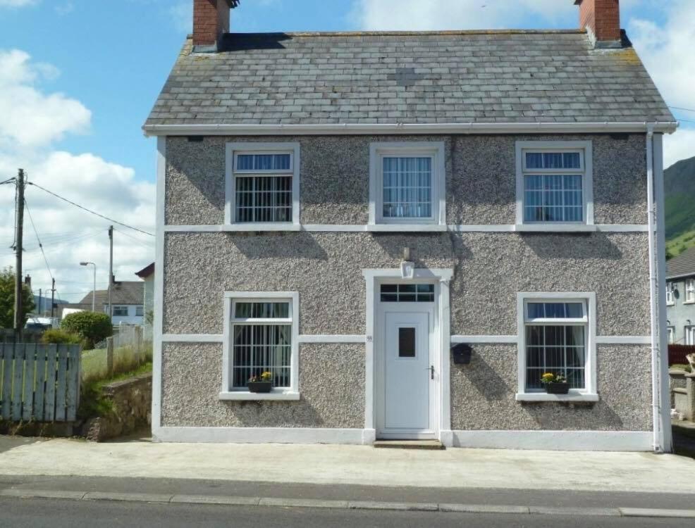 Casa de piedra con puerta blanca y ventanas en Glens of Antrim Beach House - On the Coast, en Glenariff