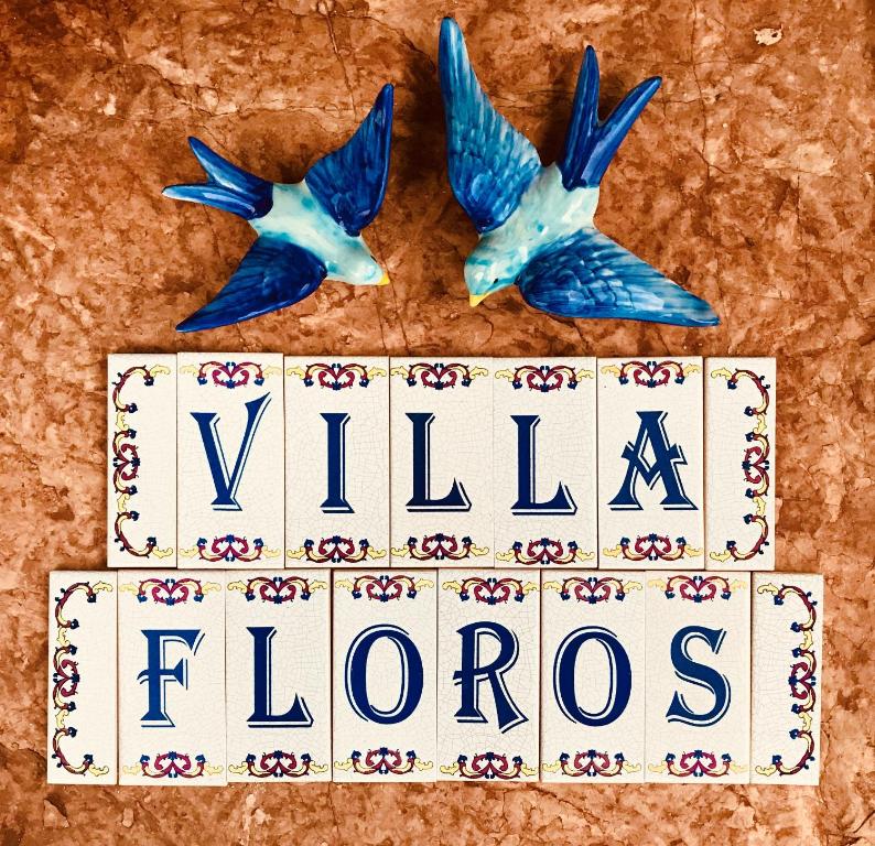 two birds flying over a sign with the word villa flores at Floros Apartments in Agios Stefanos