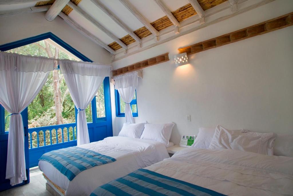 a bedroom with two beds and a window with curtains at HOTEL & CABAÑAS CASHILUNA in Villa de Leyva