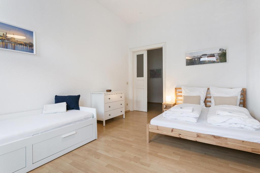 a white bedroom with two beds and a dresser at Ruhiges Apartment am Rande des Szeneviertels in Dresden