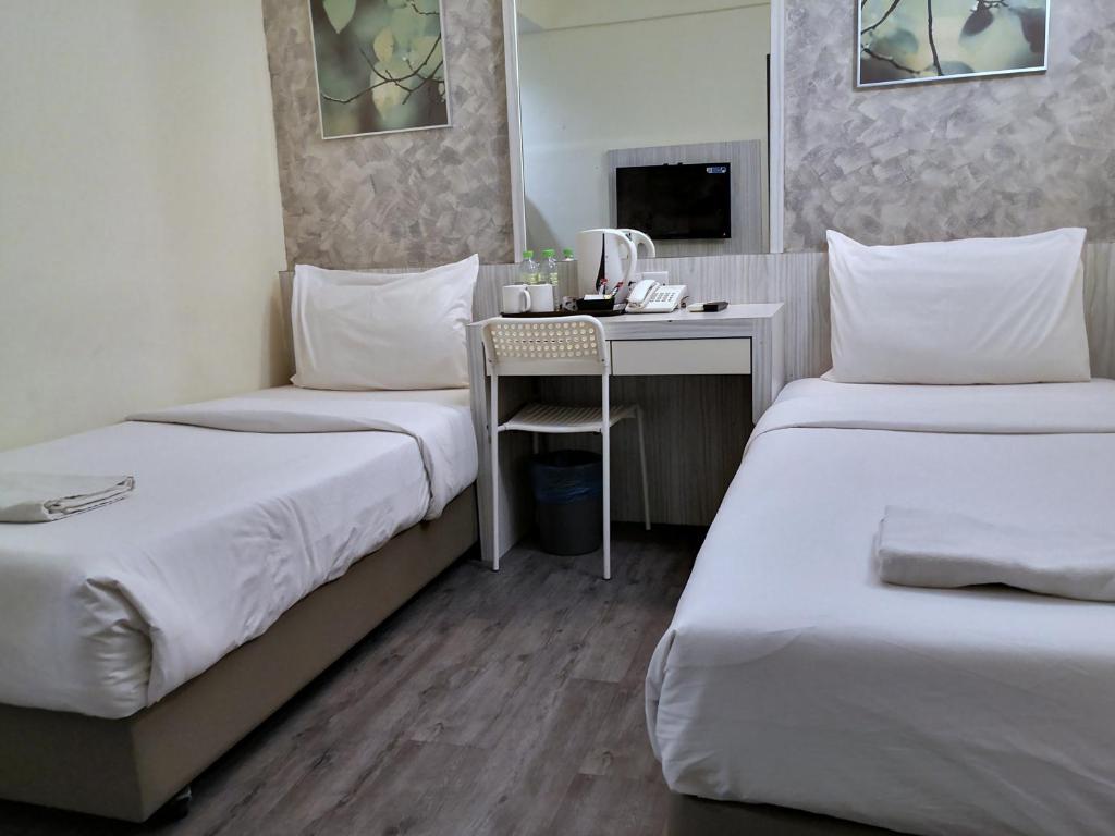 A tidy twin room with a central desk, tea-making setup, and wall-mounted television.