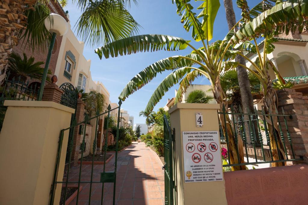 a gate with a sign next to a street with palm trees at Apartamento Nerja Medina in Nerja