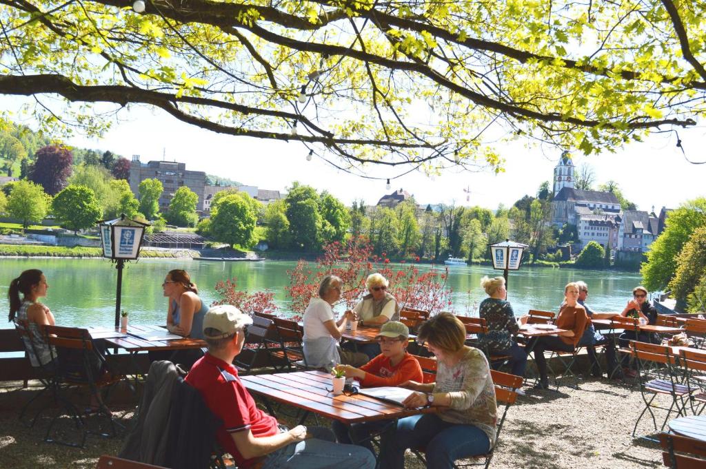 eine Gruppe von Menschen, die an Tischen in der Nähe eines Sees sitzen in der Unterkunft Alte Post - Hotel Am Rhein-Ufer Laufenburg in Laufenburg