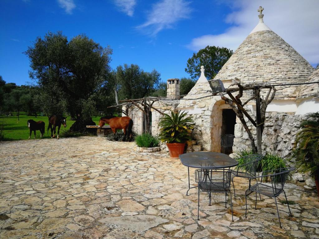 un edificio de piedra con mesa, sillas y caballos en Masseria Sciaiani Piccola en Villa Castelli