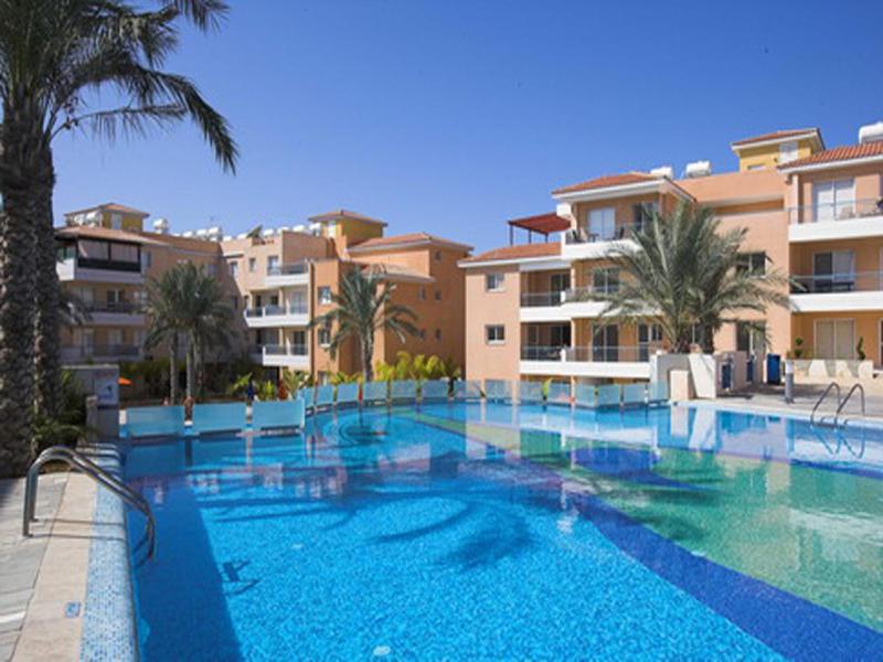 a large swimming pool with palm trees and buildings at Iris Village in Paphos