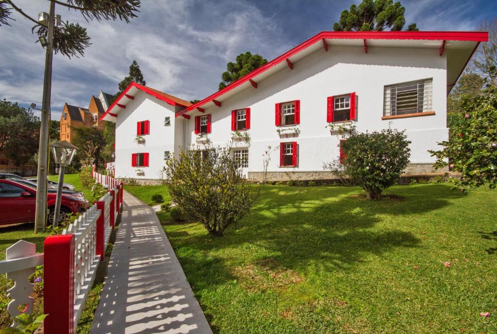 een wit huis met rode ramen en een tuin bij Jardim Nevada in Campos do Jordão