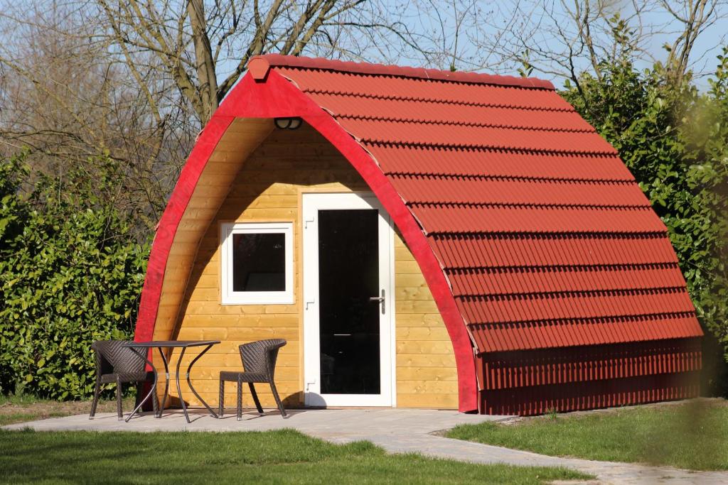 un cobertizo de techo rojo con 2 sillas y una mesa en Luxe Eco Pod op Camping de Stal, en Drijber