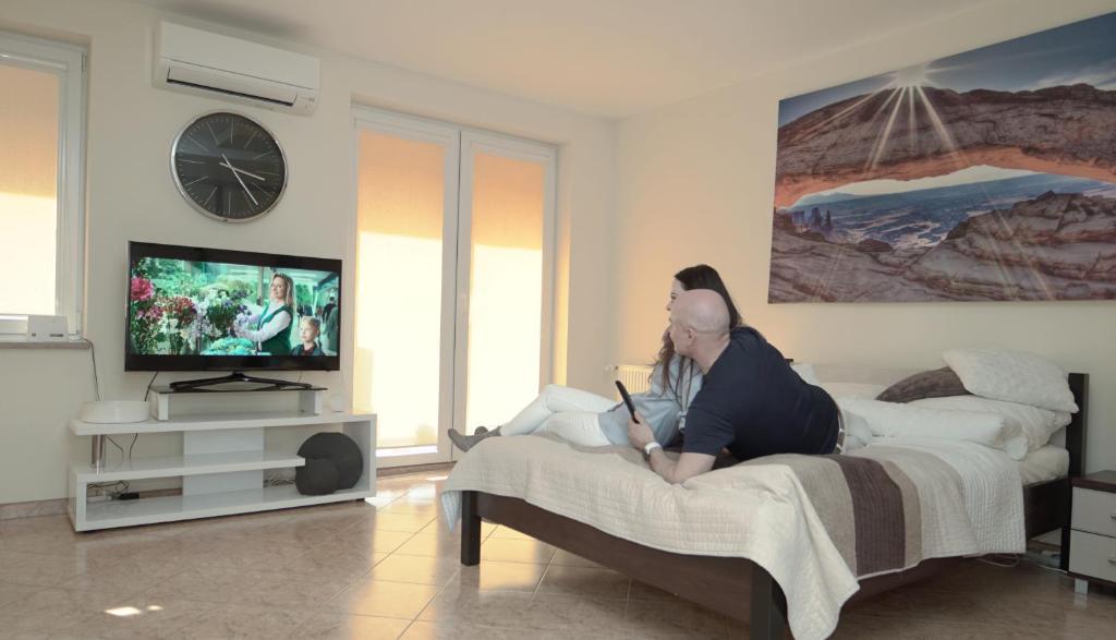 a man sitting on a bed watching a television at Apartament Zielone Tarasy 7B in Kołobrzeg