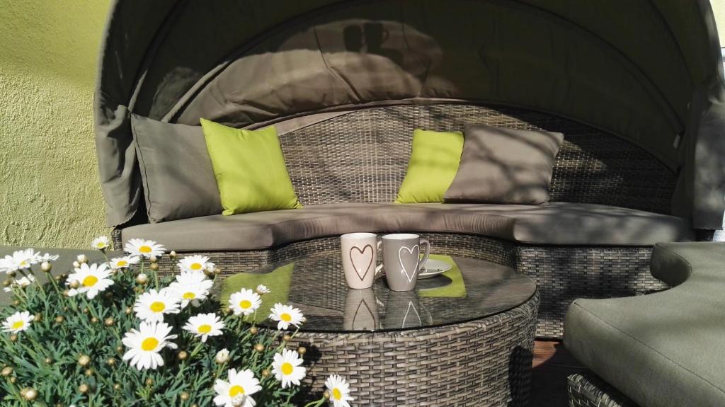 a wicker chair with green pillows and a table with flowers at Haus Liebevoll in Wald 102 in Gunzenhausen