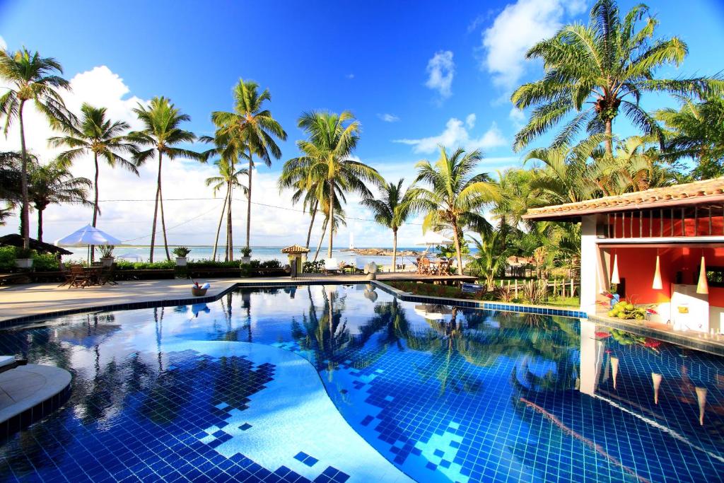 a swimming pool in front of a resort with palm trees at Aldeia do Mar Hotel in Itacaré