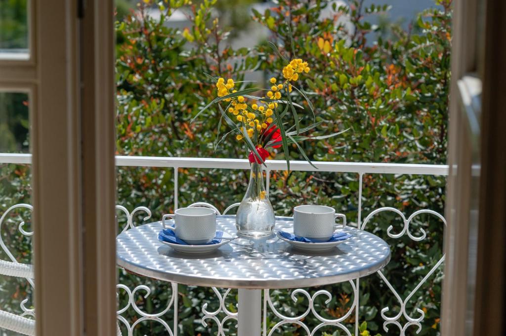 Una mesa con dos tazas y un jarrón con flores. en Mimoza, en Spetses