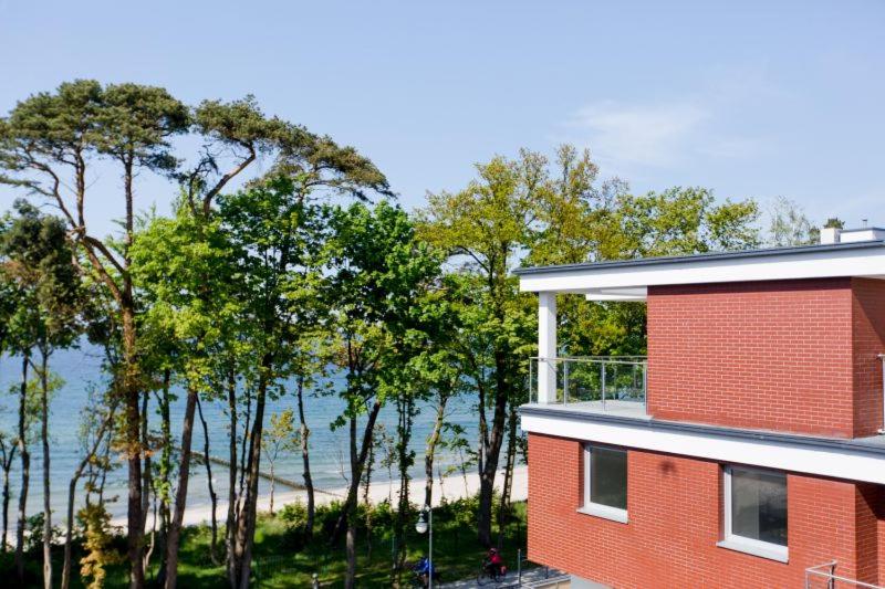 a red building with trees in front of a beach at Resort Apartamenty Klifowa Rewal 18 in Rewal
