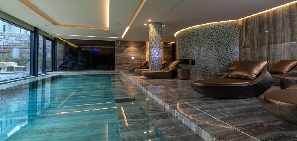 a swimming pool in a hotel with benches and chairs at Vila Foz Hotel & SPA - member of Design Hotels in Porto