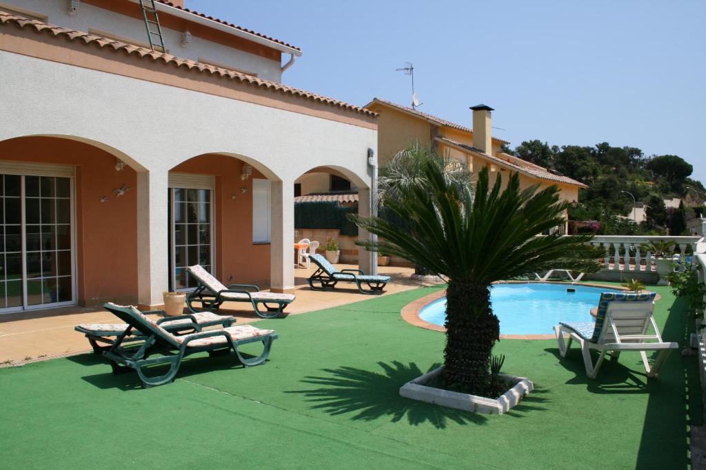 uma piscina com cadeiras e uma palmeira em frente a uma casa em Villa Costa. em Tossa de Mar