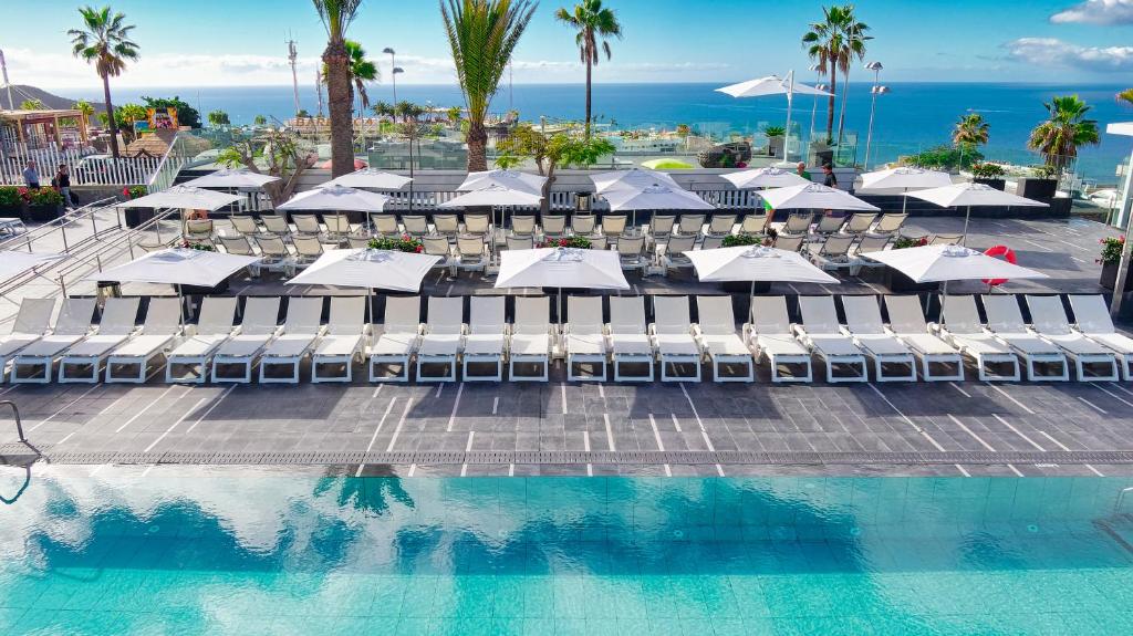 a pool with chairs and umbrellas next to the ocean at Ura Lara Adults Only in Puerto Rico de Gran Canaria