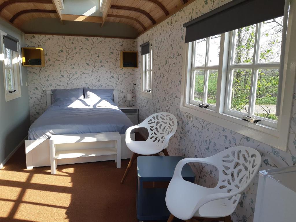 a bedroom with a bed and two white chairs at B&B Pipowagen "de Luxe" op Wellness Camping en B&B in Winterswijk-Meddo