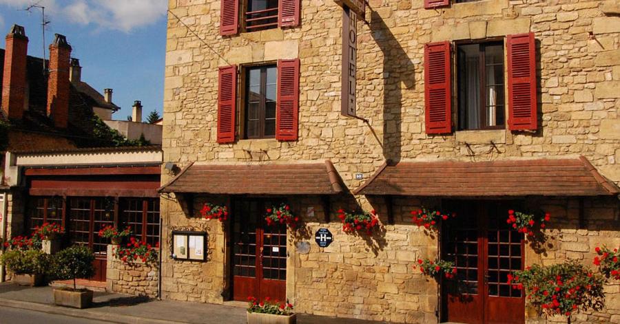 um edifício de pedra com persianas vermelhas e flores nas janelas em Hôtel Le Madrigal em Sarlat-la-Canéda