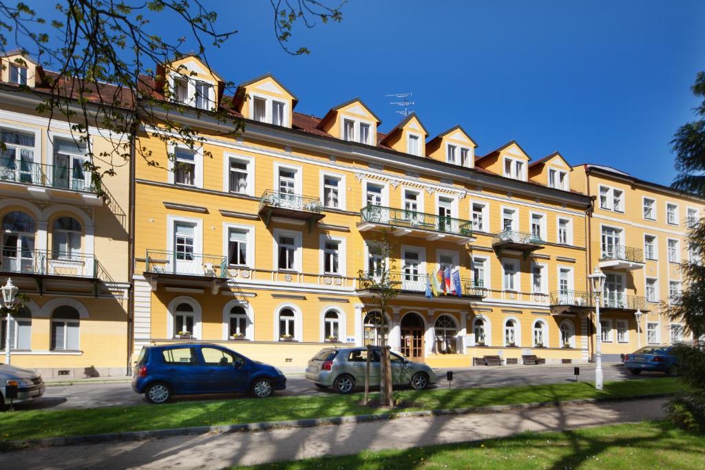 un gran edificio amarillo con coches estacionados frente a él en Dr. Adler Spa & Kurhotel en Františkovy Lázně