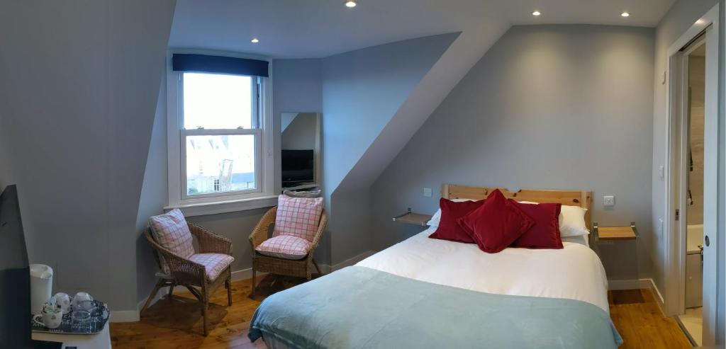 - une chambre avec un lit doté d'oreillers rouges et de 2 chaises dans l'établissement Falcon Crest Guest House, à Édimbourg