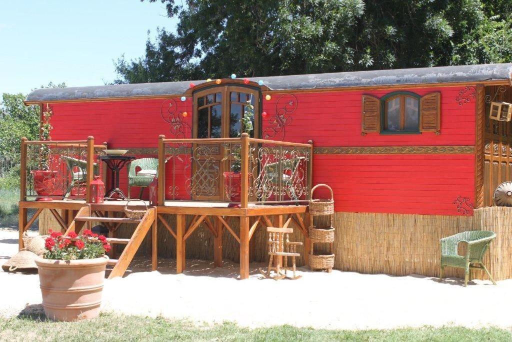 un wagon rouge avec une terrasse et une maison dans l'établissement La roulotte "Les Saintes", à Saintes-Maries-de-la-Mer