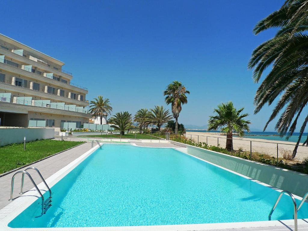 a swimming pool with palm trees and a building at Apartment Marenia by Interhome in Denia