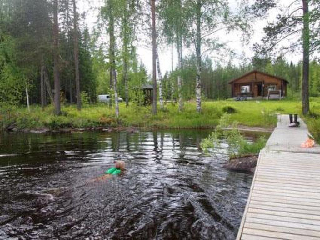 eine Person, die in einem Teich vor einer Hütte schwimmt in der Unterkunft Holiday Home Törmä by Interhome in Koivujärvi