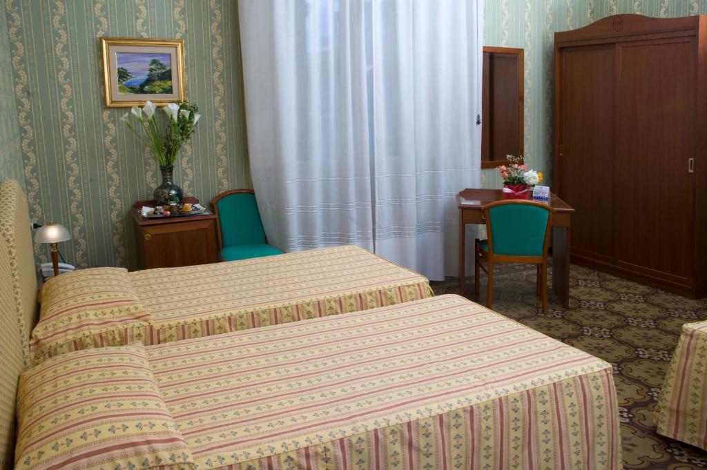 フィレンツェにあるホテル ベアトリーチェのベッド2台とテーブルが備わるホテルルームです。