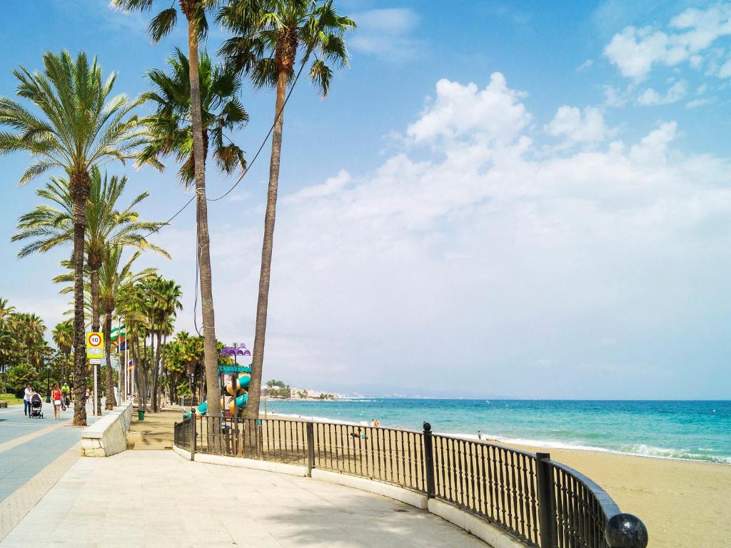 een strand met palmbomen en een hek en de oceaan bij Apartment Las Adelfas by Interhome in Marbella