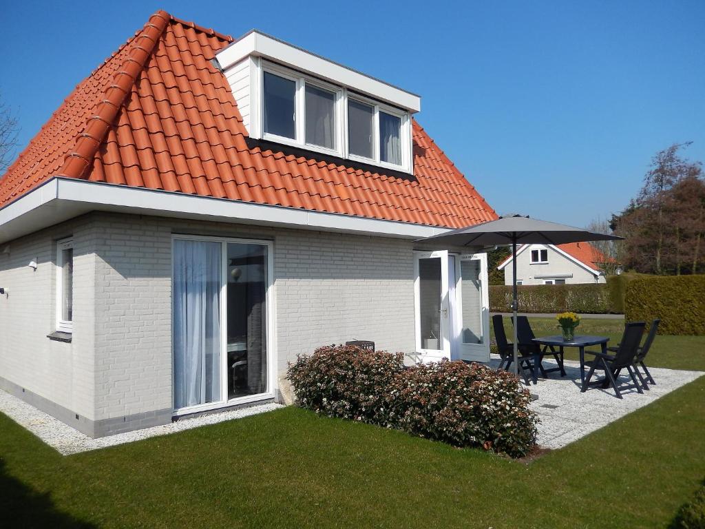 una casa con techo naranja, mesa y sombrilla en Holiday Home de Witte Raaf-3 by Interhome, en Noordwijkerhout