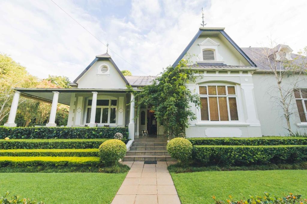 a white house with a porch and bushes at Osborne House in Pretoria