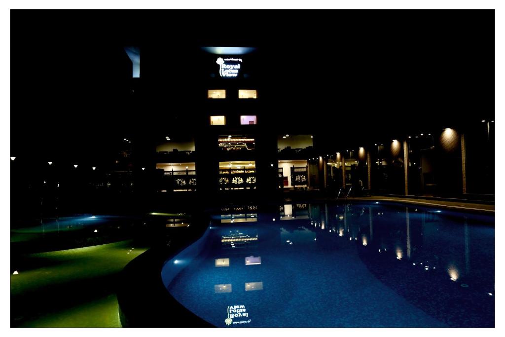 una piscina notturna con un edificio alto di Royal Lotus View Resotel a Devanhalli